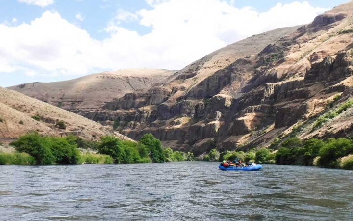 a raft is paddled by outward bound students on a calm river. There are high canyon walls surround them. 